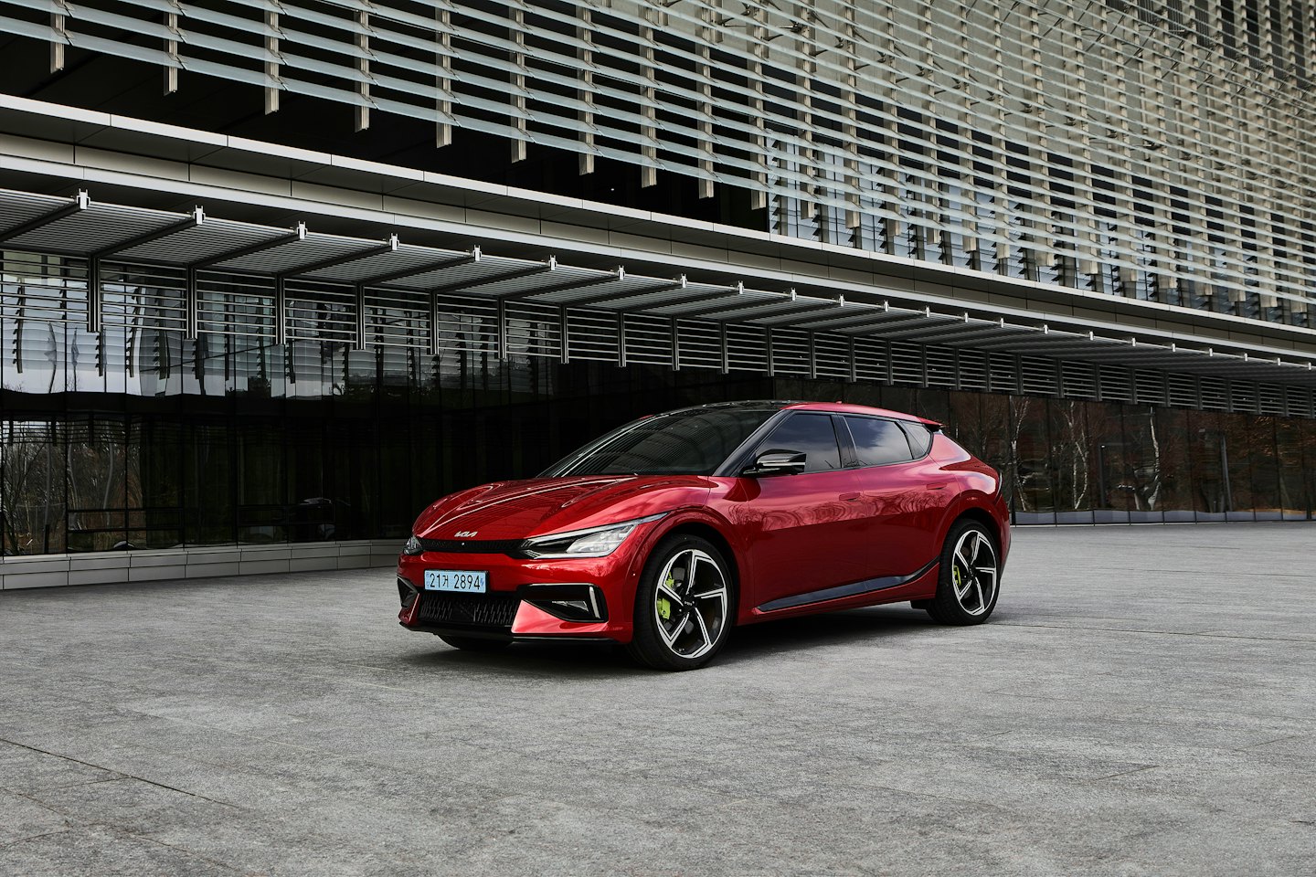 Červené elektrické auto zaparkované pred modernou budovou za slnečného dňa.